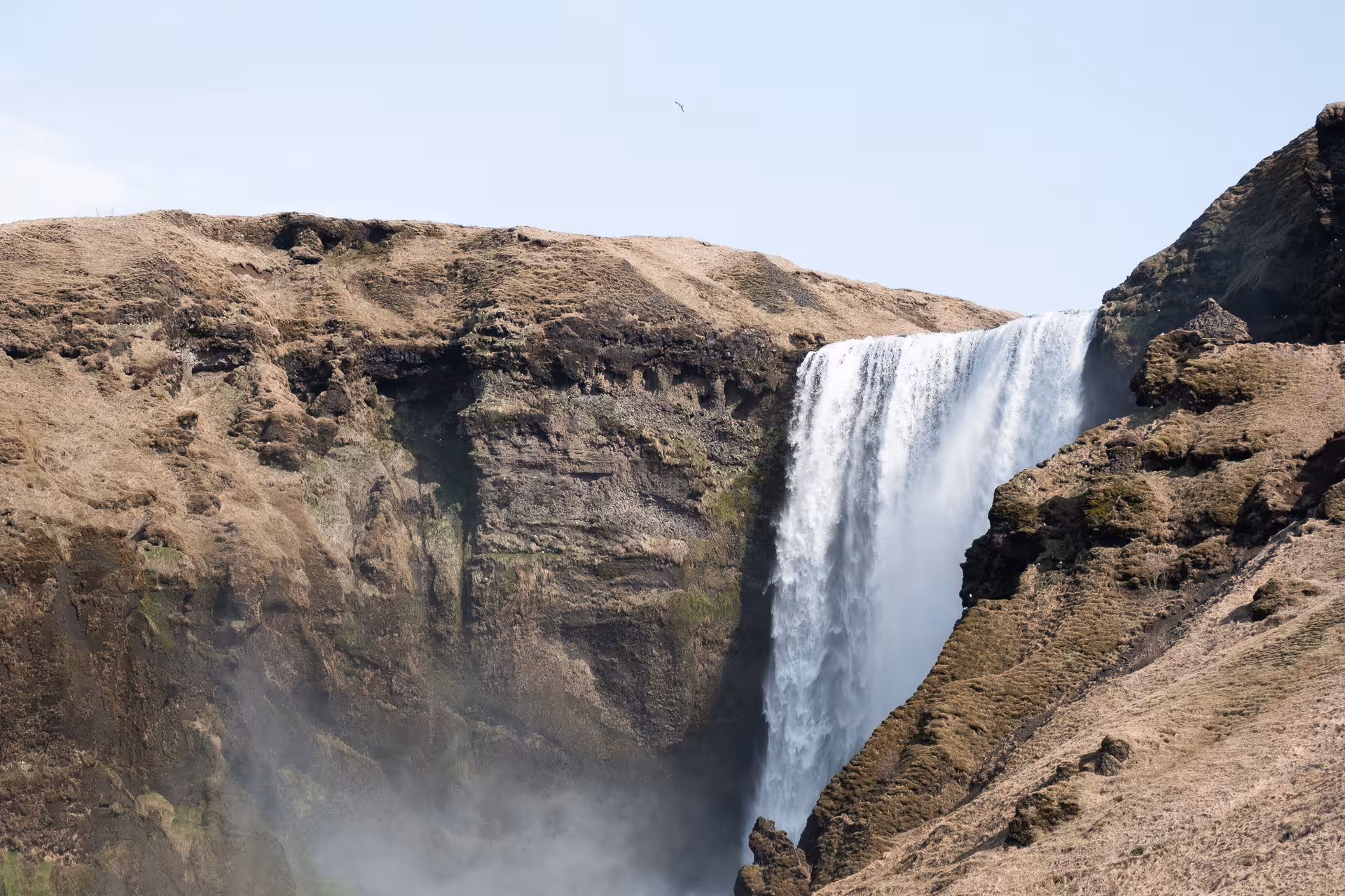 Powerful waterfall cascading down rocky cliffs on Iceland's south coast under a clear sky