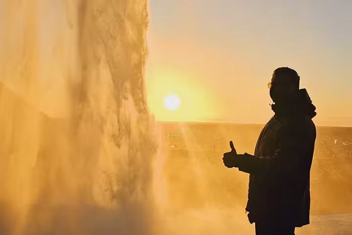 Silhouette of a person giving thumbs up beside a waterfall at golden sunset in Iceland