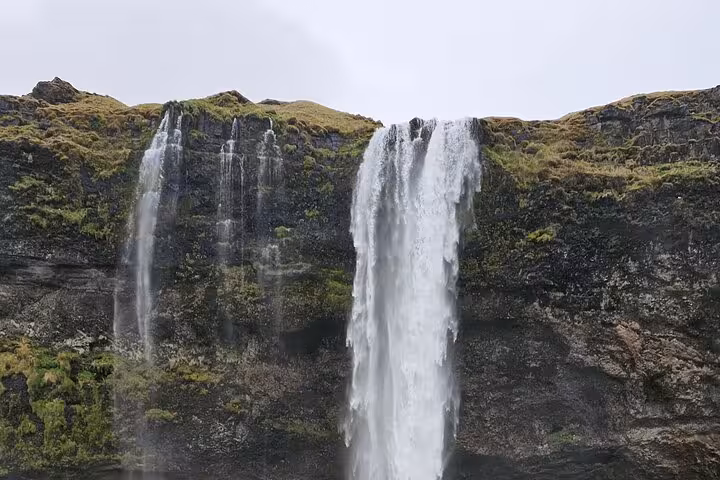 Powerful waterfall cascading down mossy black volcanic cliffs on Iceland's South Coast