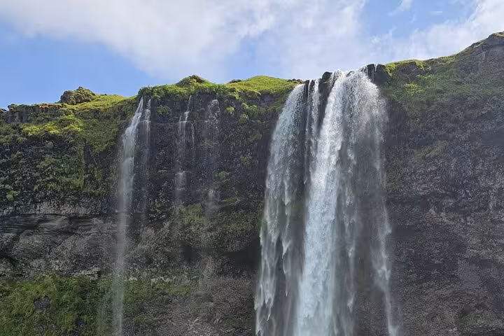 Tall waterfall cascading down mossy black volcanic cliffs on Iceland's South Coast