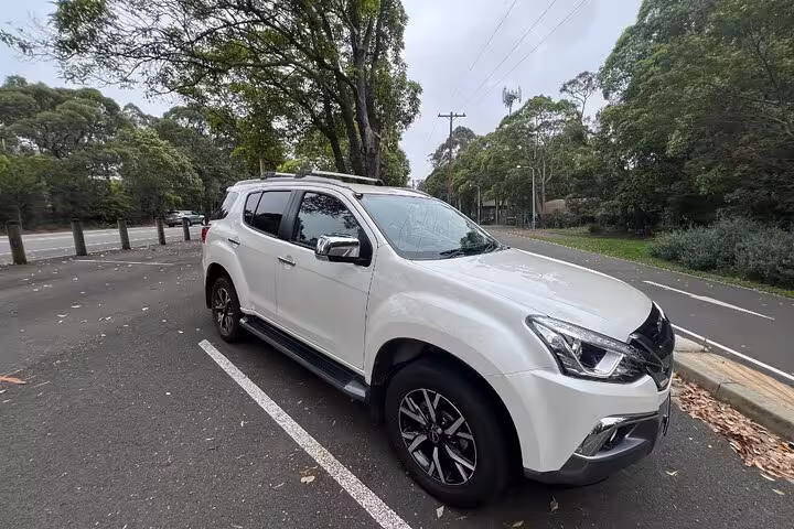 White SUV parked in a scenic, lush green setting for South Coast private daily group tour pickup.