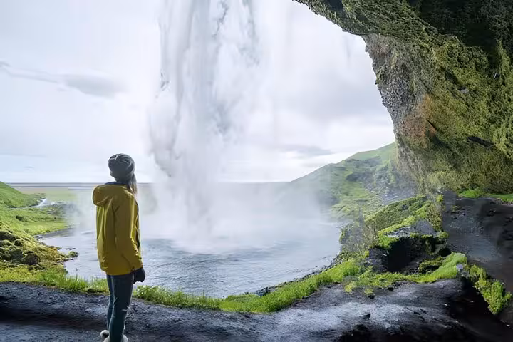 Traveler in yellow jacket standing behind Seljalandsfoss waterfall on Iceland's South Coast