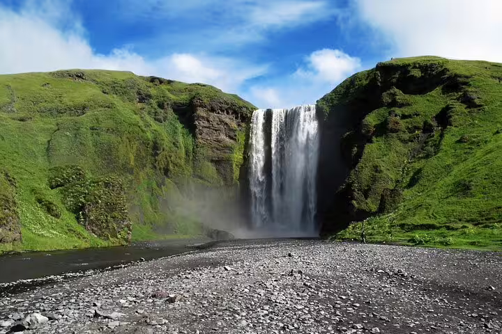 Skógafoss waterfall cascading down green cliffs onto rocky shore in Iceland's South Coast