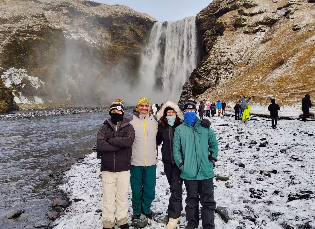 Four tourists in winter gear posing in front of Skógafoss waterfall on Iceland's South Coast