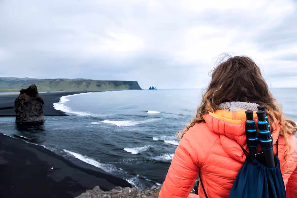 Hiker in red jacket overlooking Iceland's black sand beach with sea stacks on South Coast