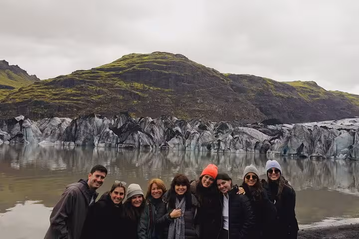 Group of tourists posing in front of a glacier lagoon and volcanic mountain on Iceland's South Coast