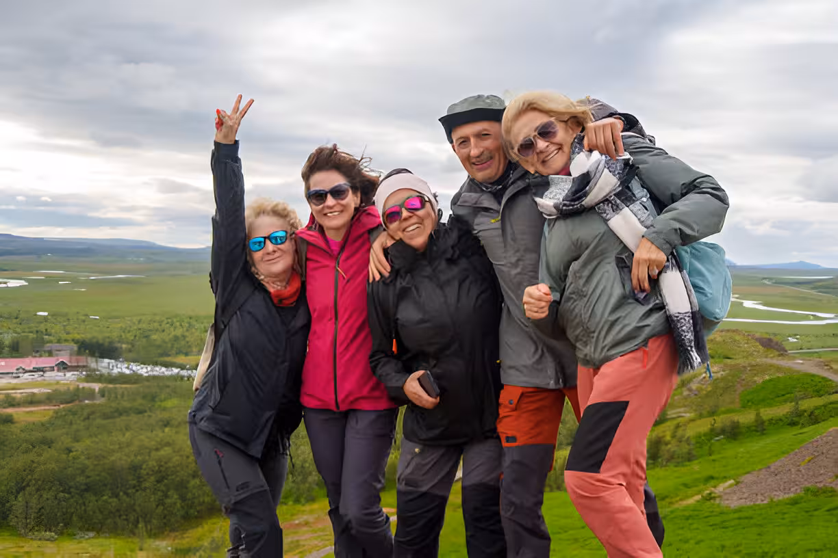 Group of five happy hikers posing on a hilltop with a vast green Icelandic valley below