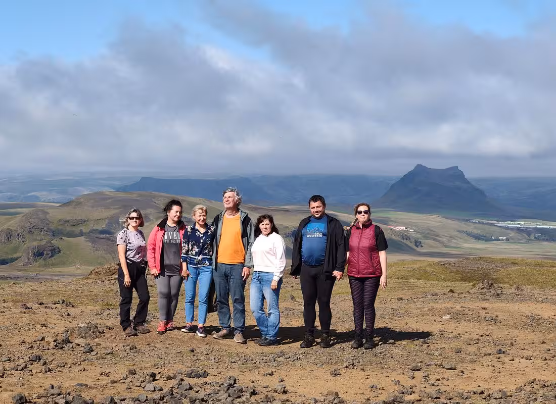 Group of seven tourists posing on a hilltop with Iceland's dramatic volcanic landscape and mountains behind