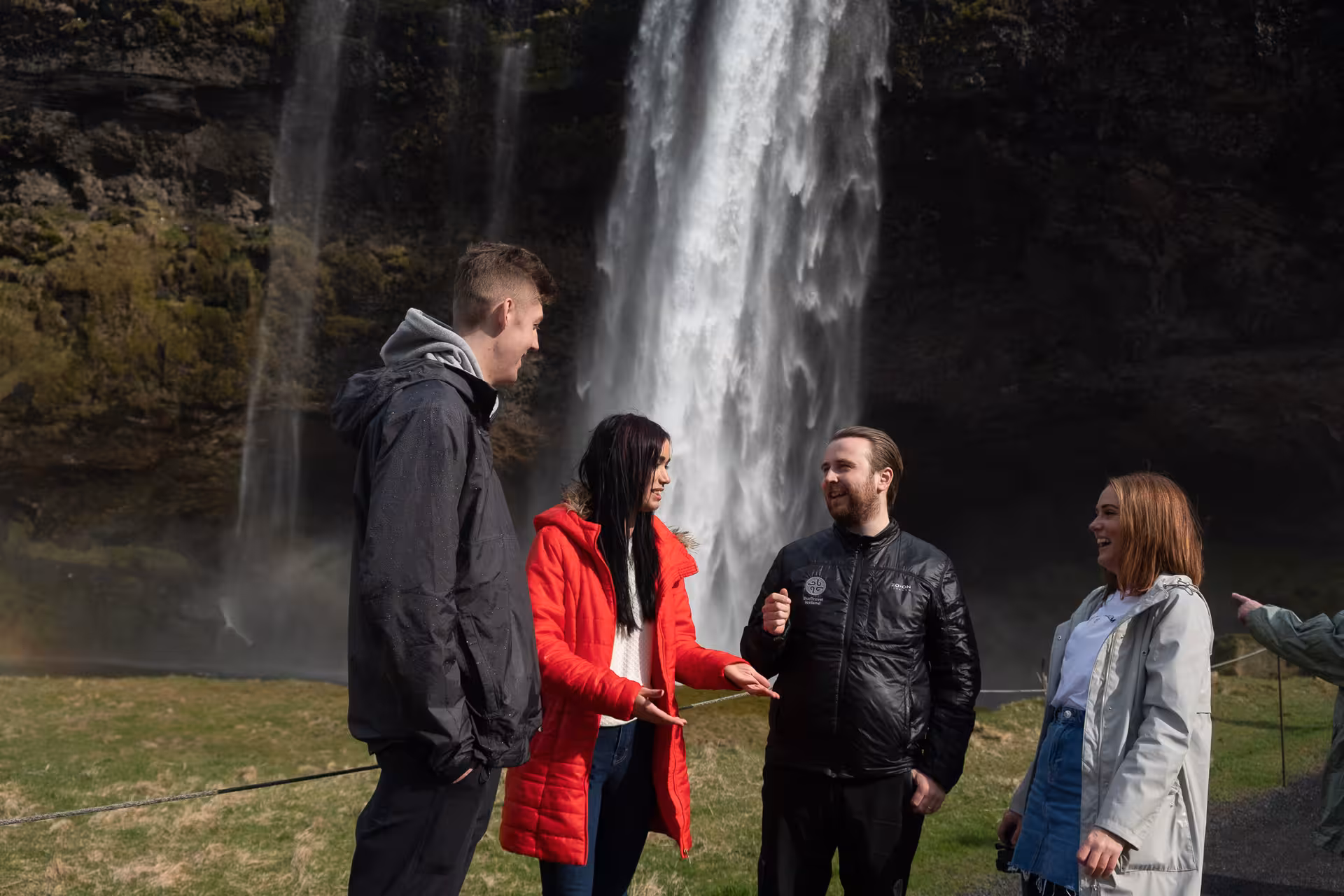 Four tourists conversing in front of Seljalandsfoss waterfall on Iceland's south coast