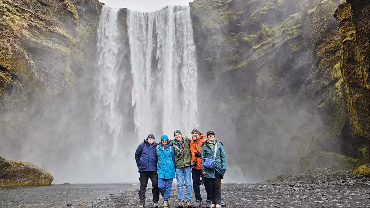 Group of five tourists posing in front of Skógafoss waterfall on Iceland's South Coast