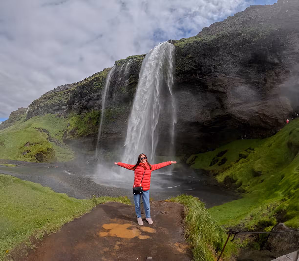 Woman in red jacket posing with arms wide open in front of Seljalandsfoss waterfall on Iceland's South Coast