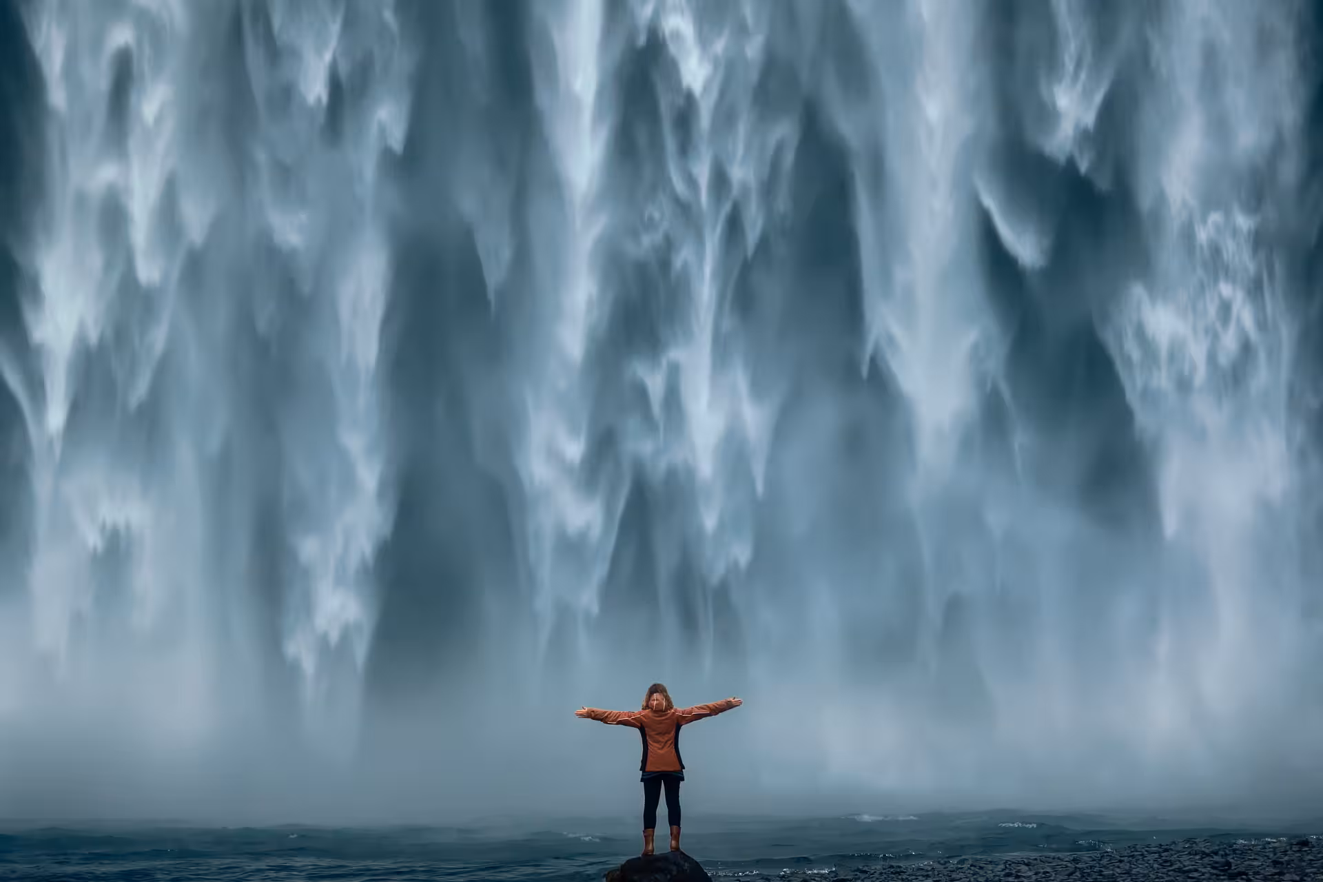 Person with arms outstretched standing before massive Skógafoss waterfall on Iceland's South Coast