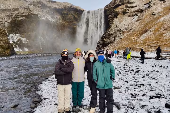Four tourists in winter gear posing in front of Skógafoss waterfall on Iceland's snowy South Coast