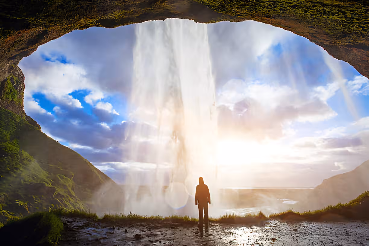 Silhouette of person standing behind massive waterfall viewed from cave on Iceland's South Coast