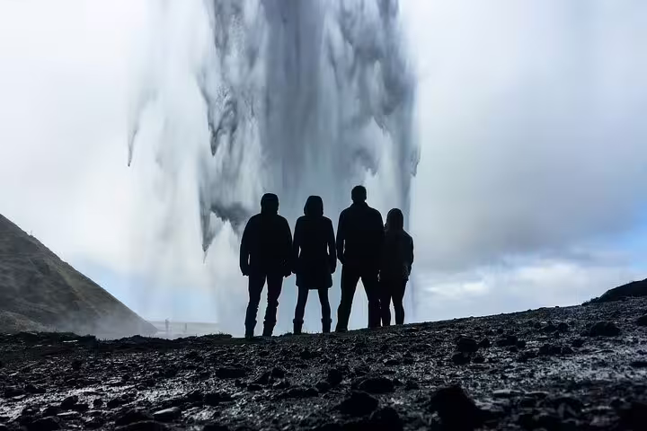 Four silhouetted visitors standing before a massive waterfall on Iceland's south coast