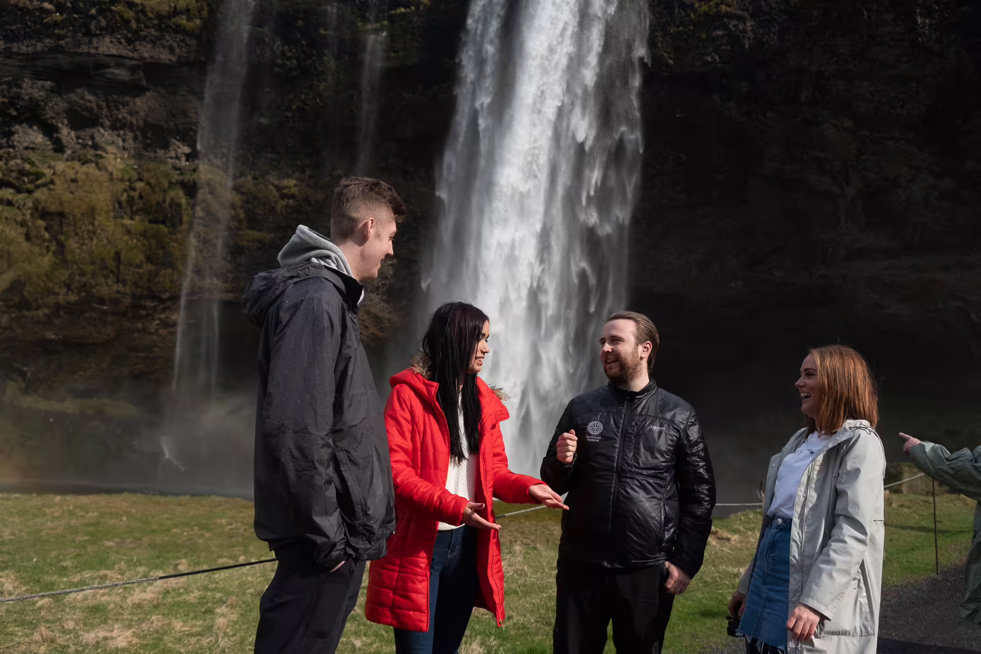 Four tourists talking and laughing in front of Seljalandsfoss waterfall on Iceland's South Coast