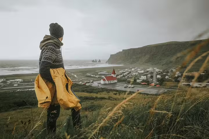 Traveler overlooking Vík village, black sand beach, and red church from hillside on Iceland's South Coast