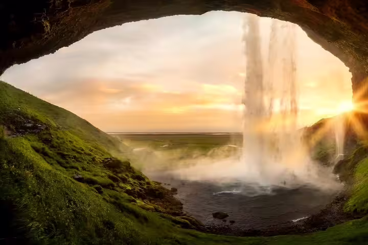 View from behind Seljalandsfoss waterfall at golden sunset on Iceland's south coast