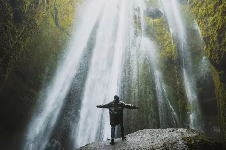 Person standing with arms outstretched before a cascading waterfall in a mossy canyon on Iceland's South Coast