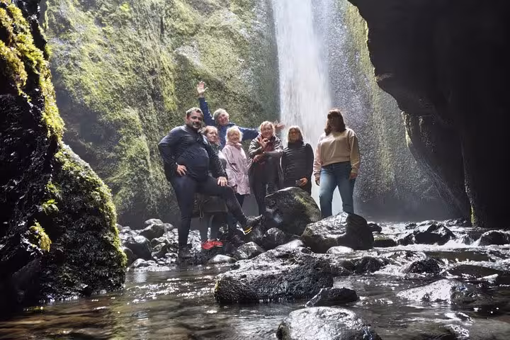 Group of tourists posing inside a mossy cave beside a waterfall on Iceland's South Coast