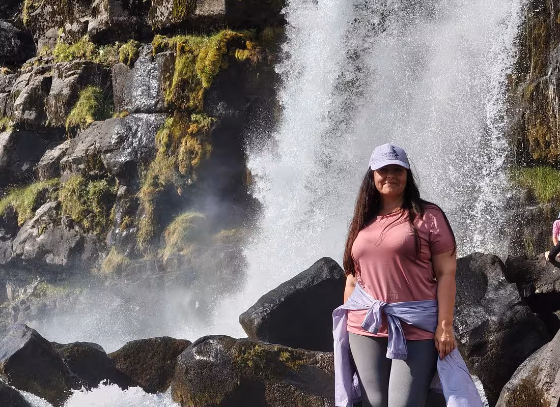 Woman in pink shirt posing in front of a powerful waterfall on Iceland's South Coast