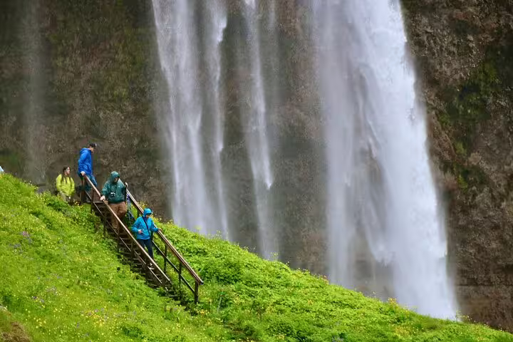Hikers climbing steep stairs on green hillside beside Seljalandsfoss waterfall in Iceland
