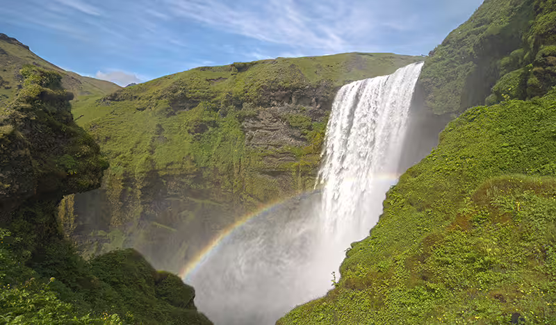 Skógafoss waterfall on Iceland's South Coast with a vivid rainbow in the mist surrounded by green cliffs