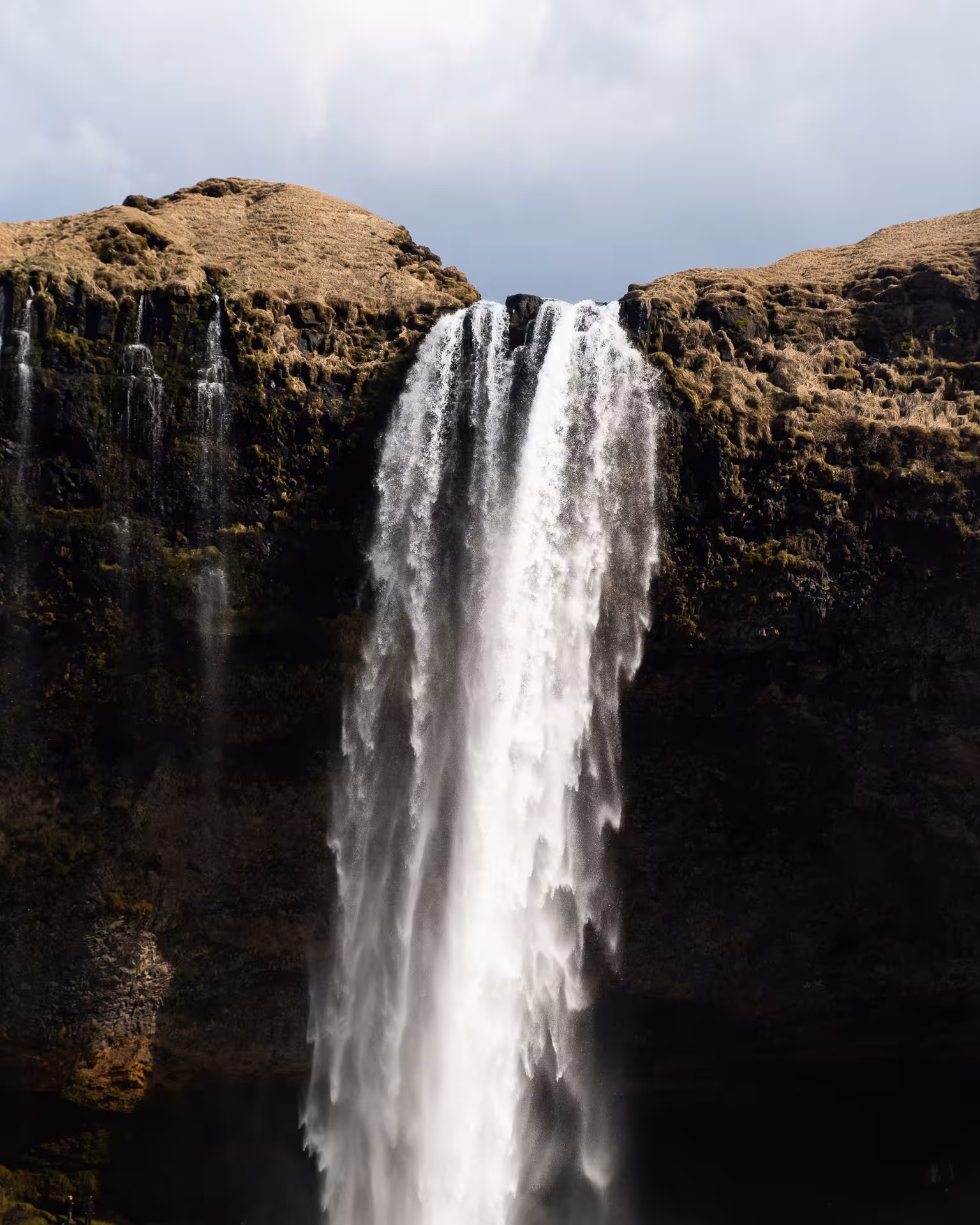 Tall waterfall cascading down dark volcanic cliffs on Iceland's South Coast