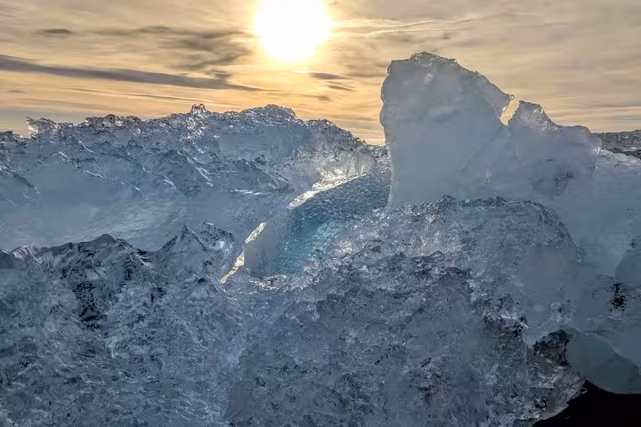 Translucent glacial ice chunks on black sand beach with golden sunset sky in South East Iceland
