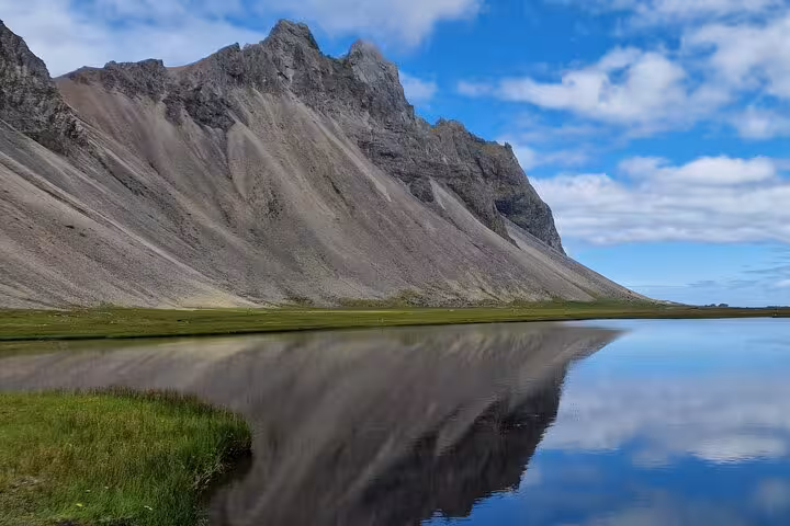 Dramatic rocky mountain reflecting in calm lagoon waters under blue sky in South East Iceland