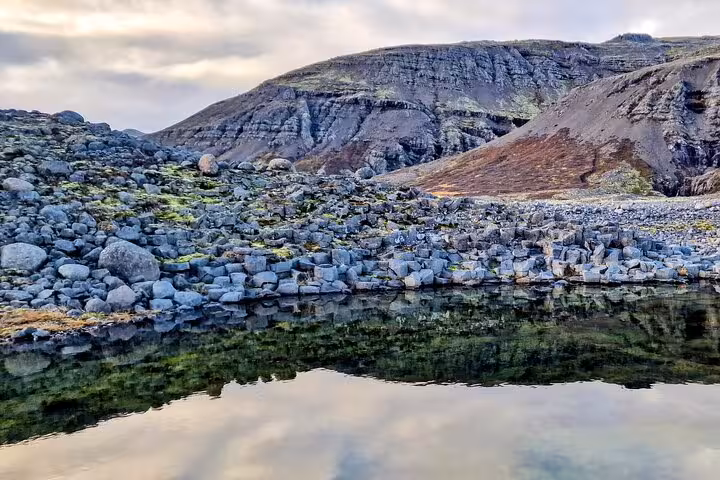 Rocky volcanic shoreline reflecting calm water with layered cliffs in South East Iceland