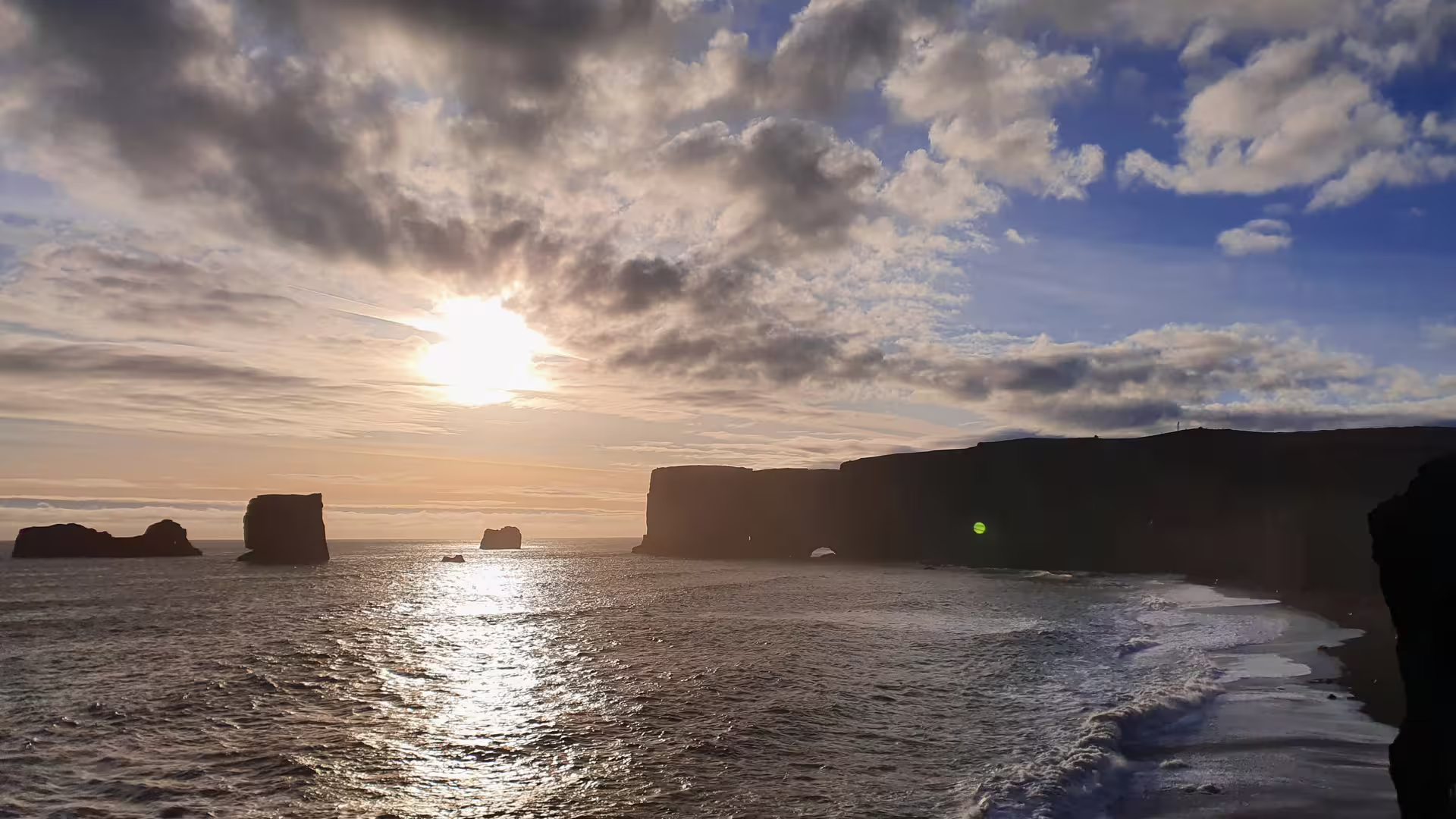 Black sand beach with dramatic sea stacks and rocky arch at sunset, South Iceland coastline