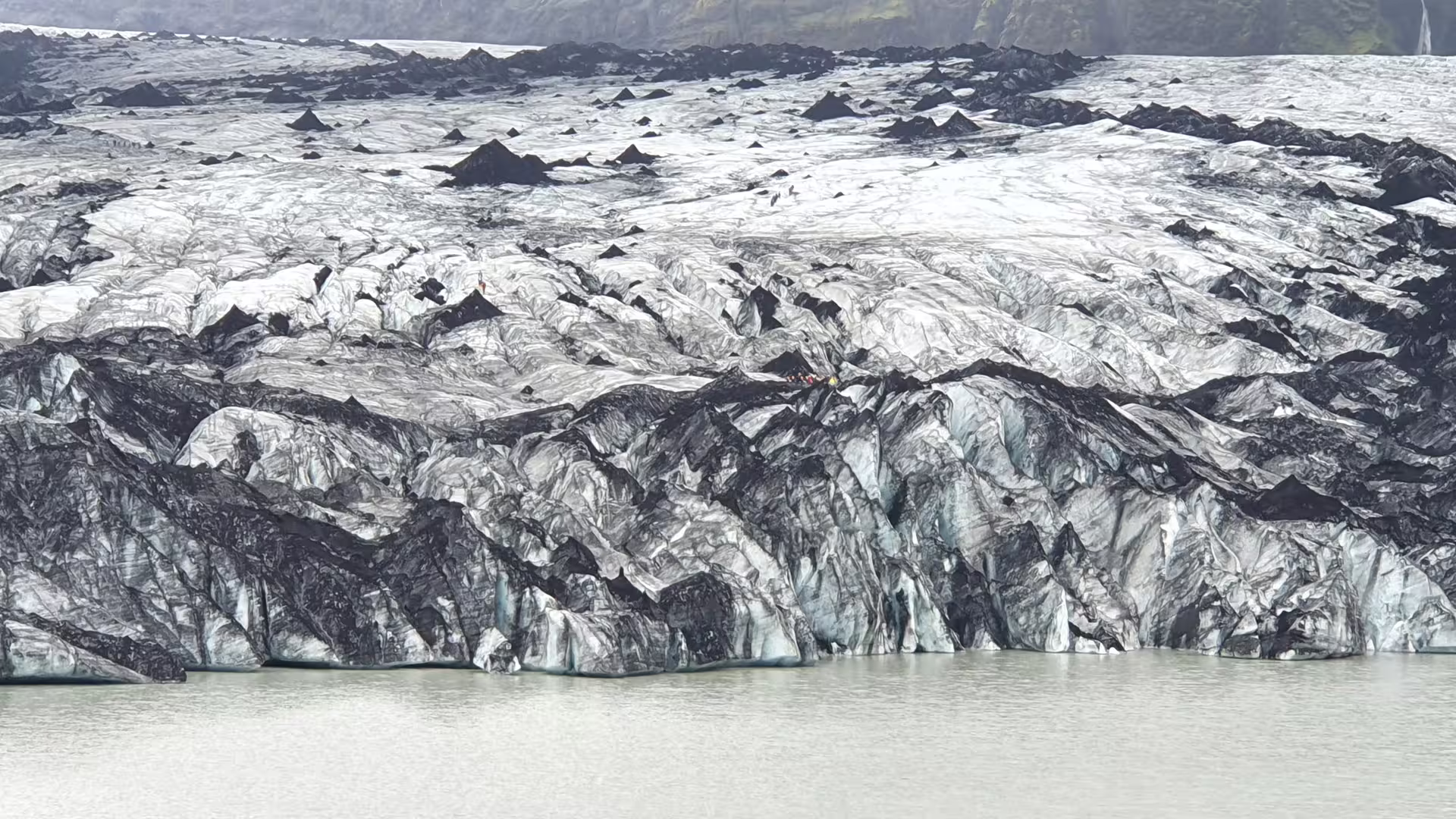 Black volcanic ash-covered glacier with icy blue seracs meeting a glacial lagoon in South Iceland