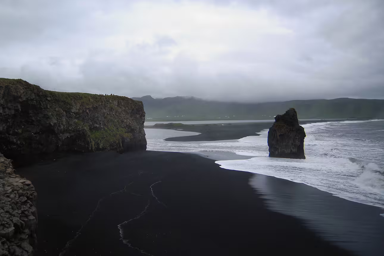 Black sand beach with dramatic sea stack and coastal cliffs on Iceland's south coast under overcast skies