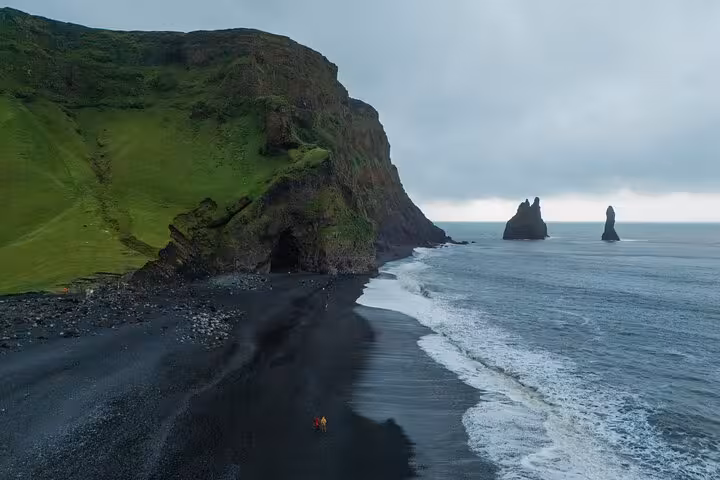 Black sand beach with sea stacks and green cliffs in South Iceland on a cloudy day