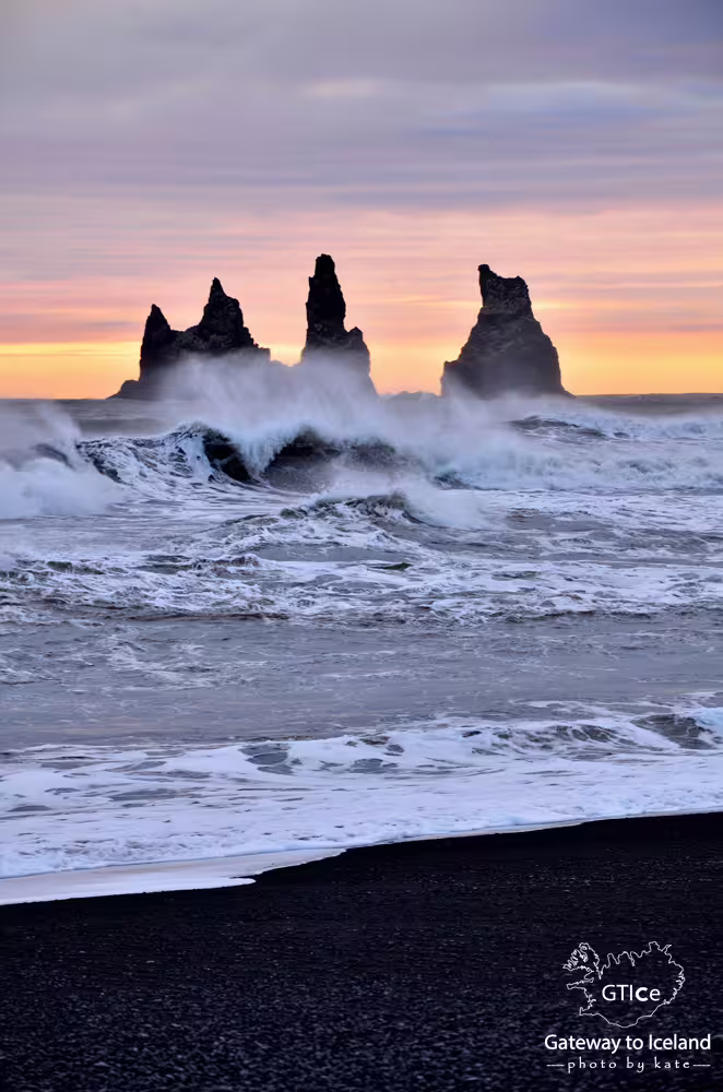 Black sand beach with dramatic sea stacks at sunset, crashing waves on Iceland's south coast