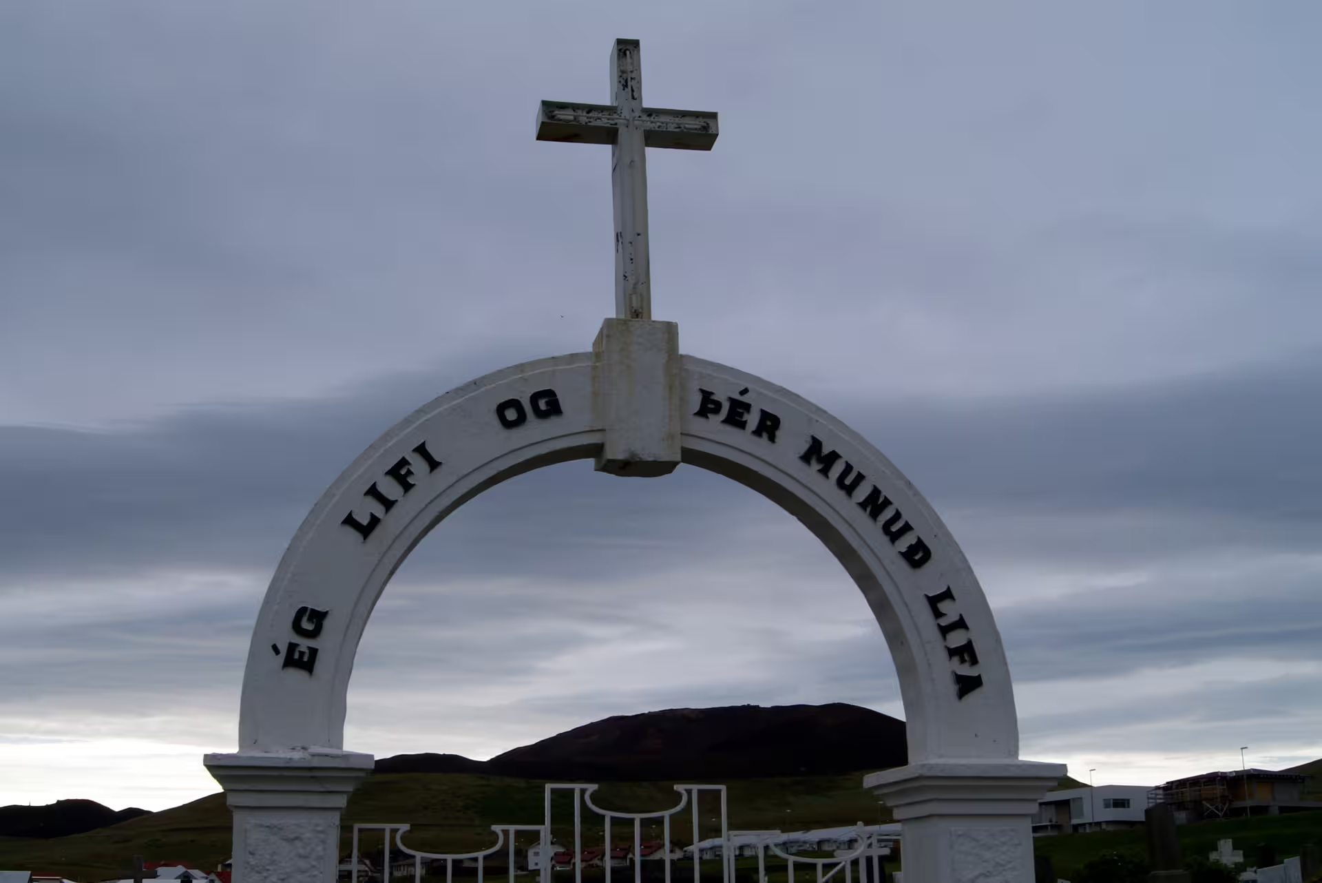 White arch gateway with Christian cross and Icelandic inscription at South Iceland cemetery entrance