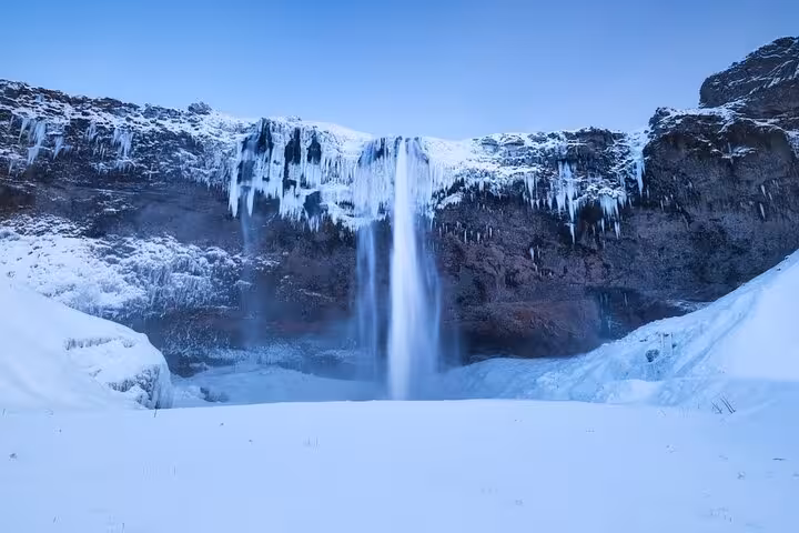 Seljalandsfoss waterfall frozen in winter with snow-covered ground and icicles on cliffs in South Iceland