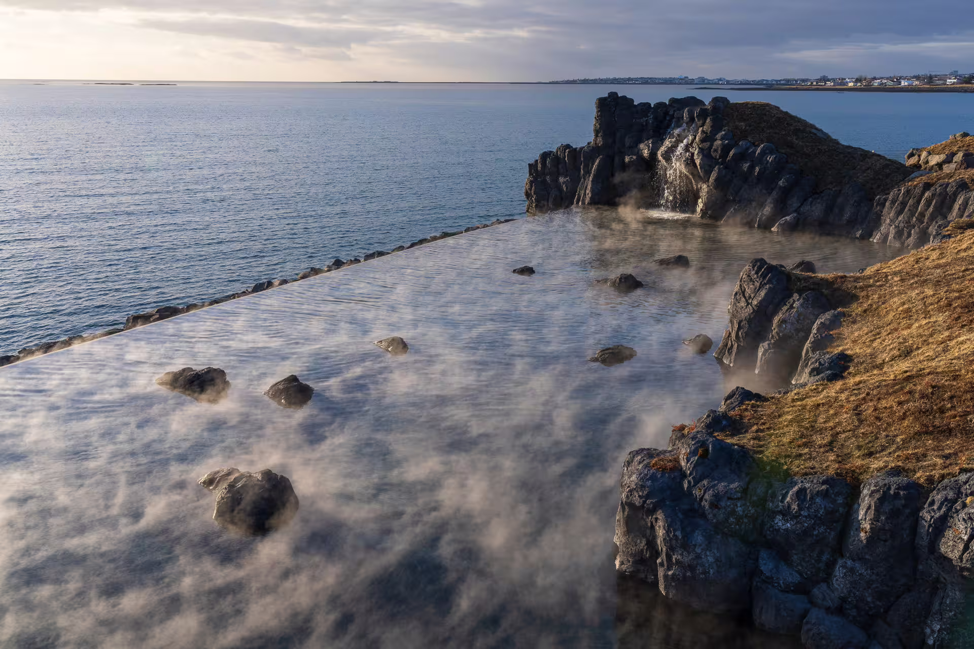 Steaming geothermal infinity pool overlooking the ocean with volcanic rocks on Iceland's south coast