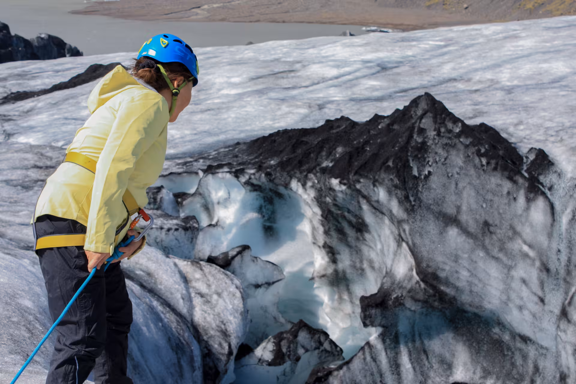 Hiker in yellow jacket and blue helmet rappelling into glacial crevasse on South Iceland glacier hike