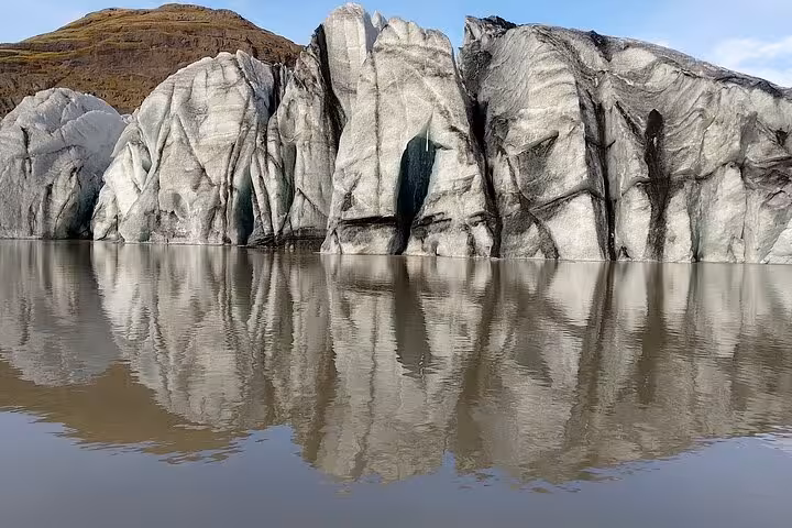 Glacier ice formations with dark volcanic streaks reflecting in a glacial lagoon in South Iceland