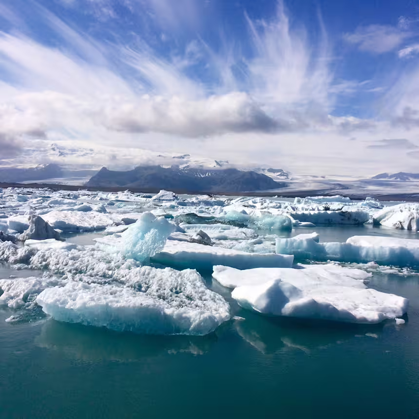 Floating icebergs in Jökulsárlón Glacier Lagoon with snow-capped mountains under a blue sky, South Iceland.