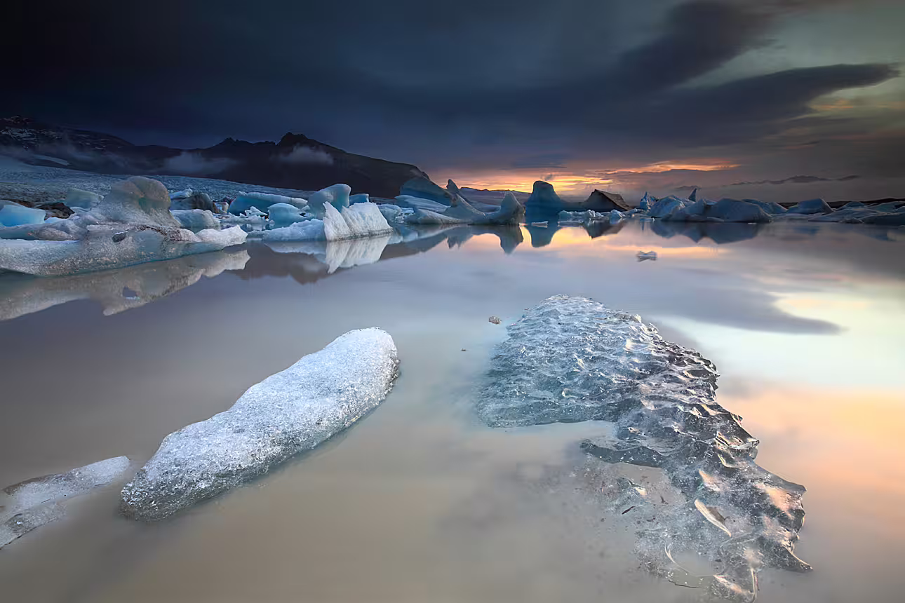 Icebergs floating on Jökulsárlón glacier lagoon at sunset with dramatic storm clouds in South Iceland
