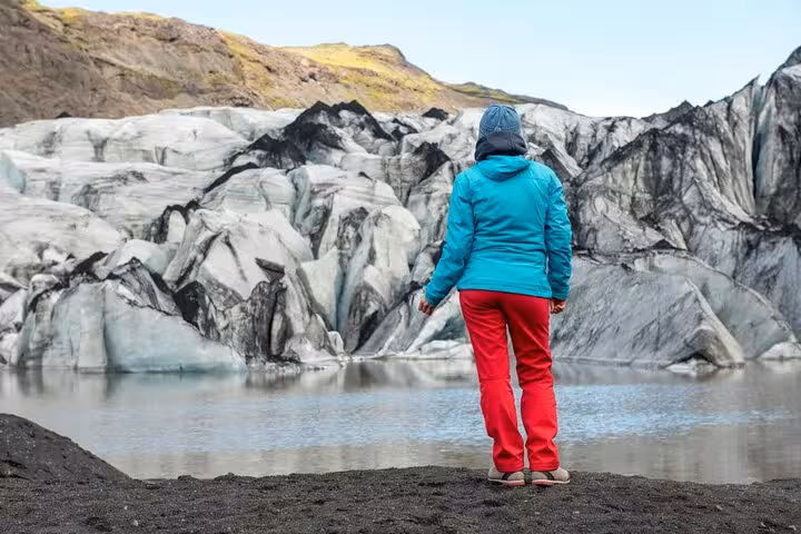 Traveler in teal jacket standing before glacier and glacial lagoon in South Iceland
