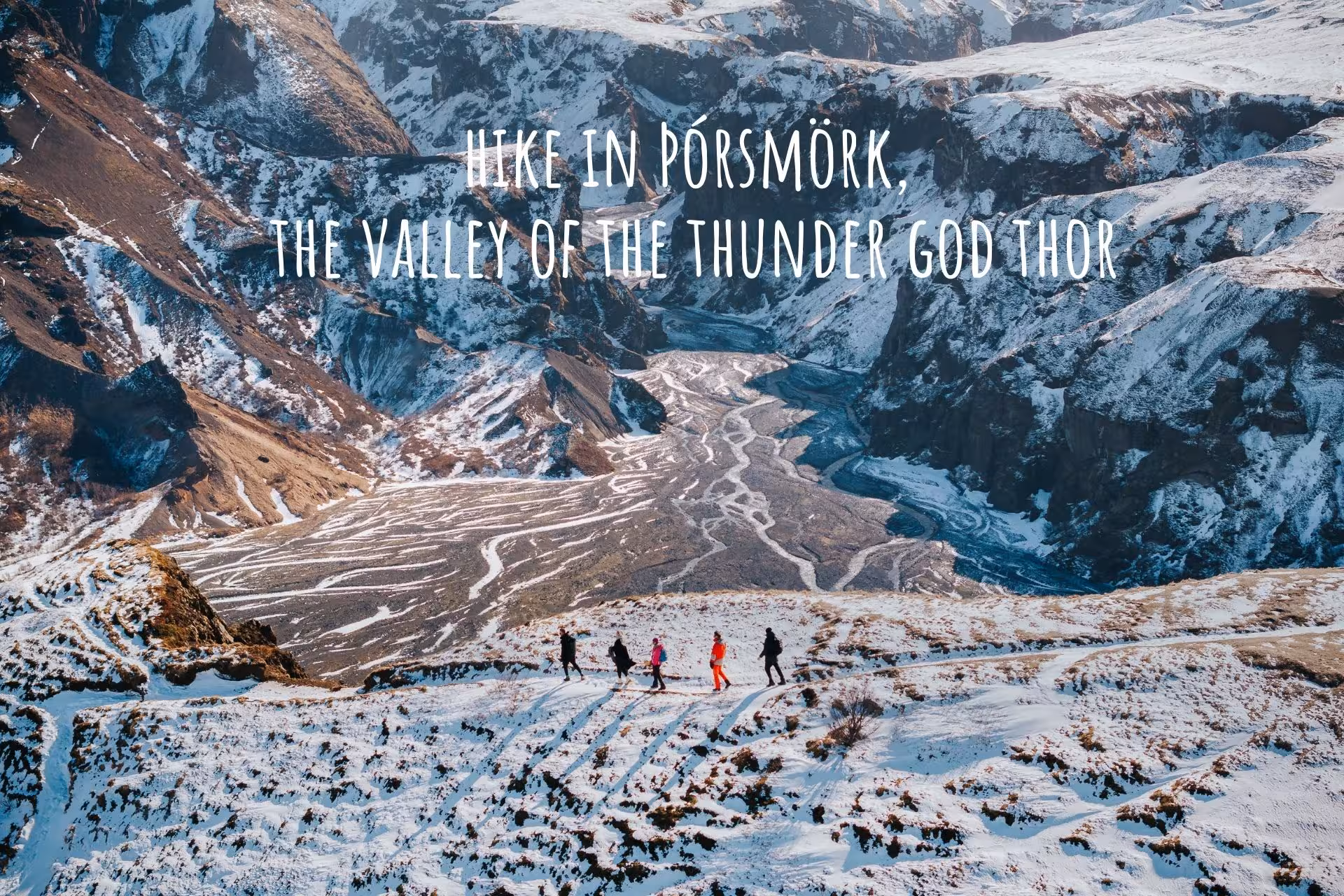 Hikers trekking snowy Þórsmörk valley with braided glacial river and mountain peaks in Iceland