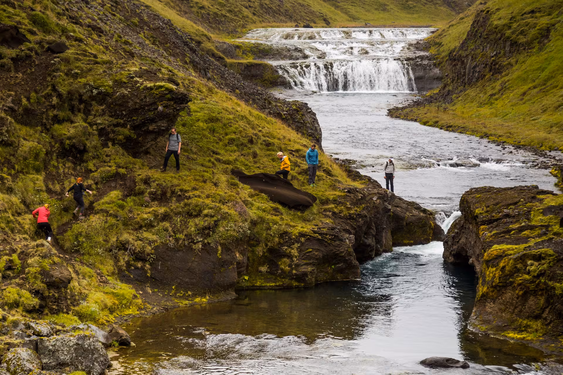 Hikers exploring a mossy canyon with cascading waterfalls in South Iceland