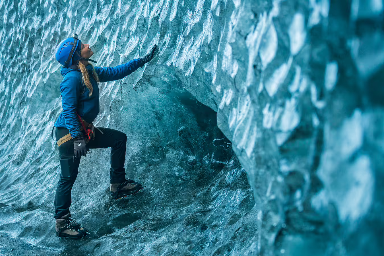 Woman in blue gear exploring a glacial ice cave with crampons and helmet in Iceland