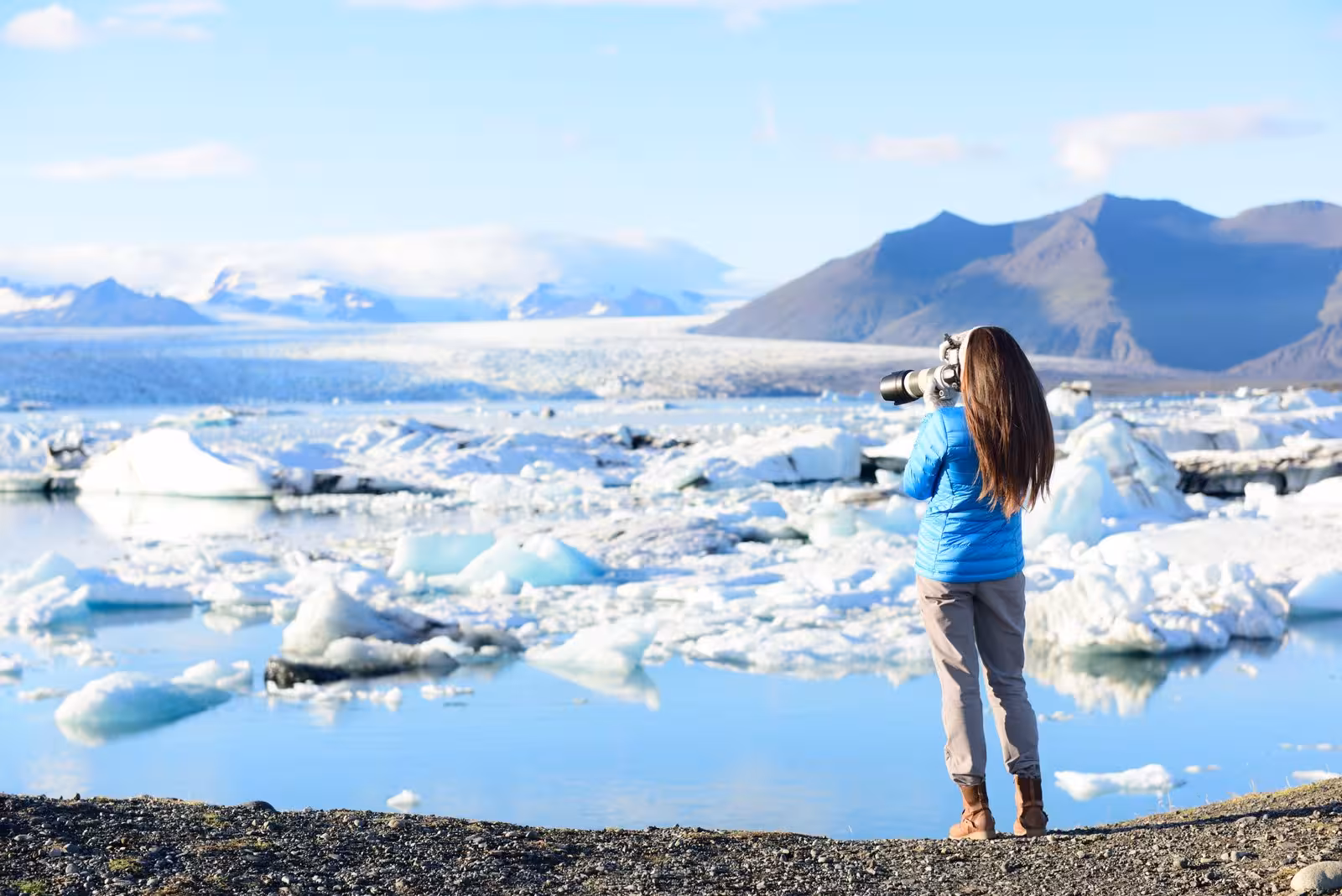 Traveler photographing icebergs at Jökulsárlón Glacier Lagoon, capturing South Iceland's breathtaking natural beauty.