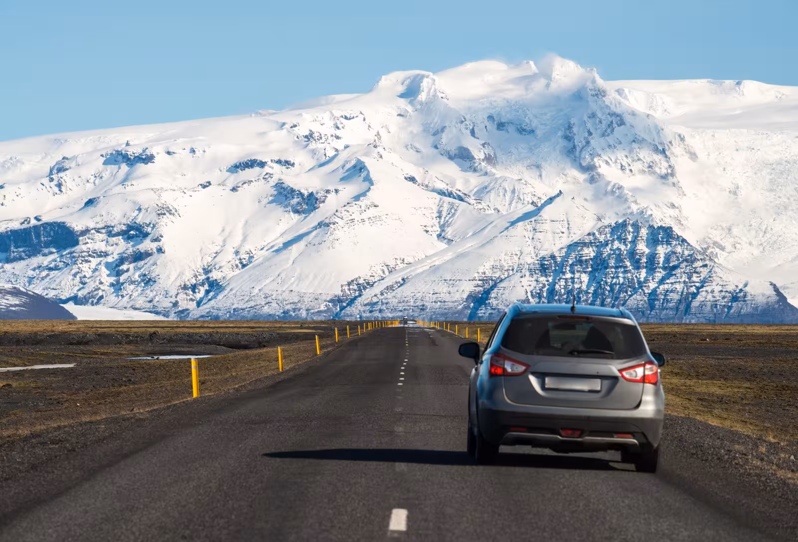 Car drives towards snow-capped mountains on a scenic road in South Iceland during a self-drive tour.