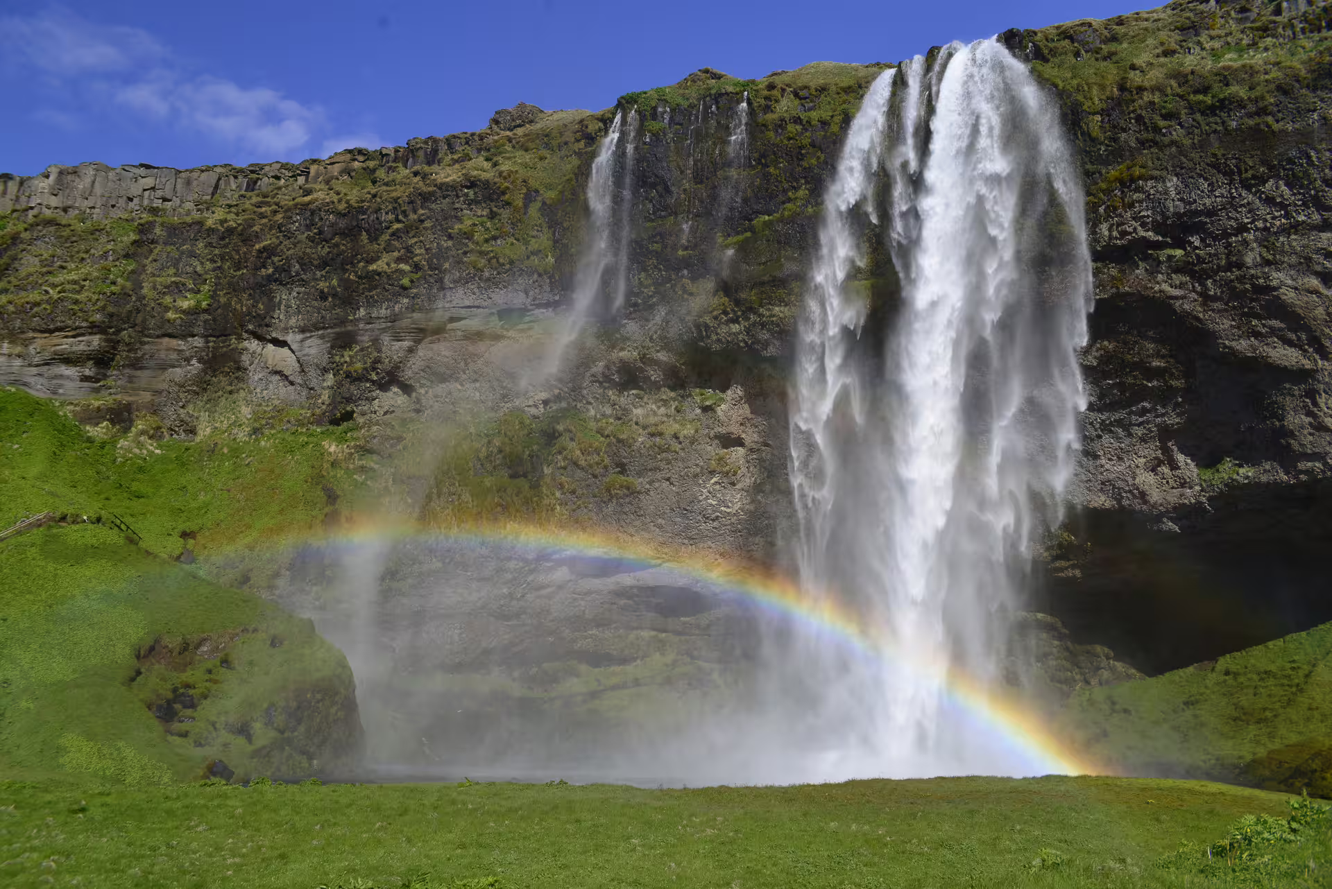 Majestic Seljalandsfoss waterfall in South Iceland with a double rainbow over lush green landscape
